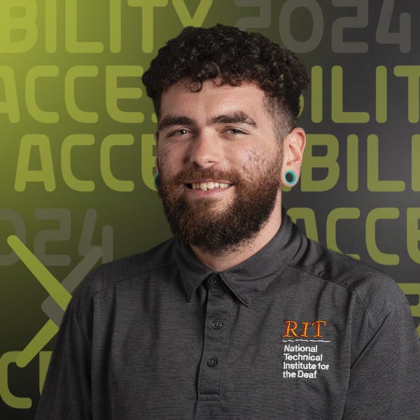 Headshot of Dyl in a dark grey polo with the RIT logo on the lapel standing against a dark grey background