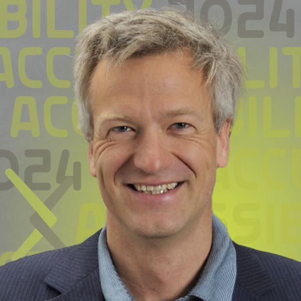 Headshot of Norbert in a blue shirt and blazer smiling against a grey background